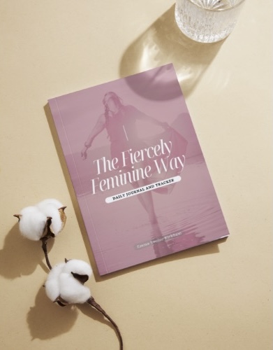 Journal on a desk besides a glass of water and some flowers