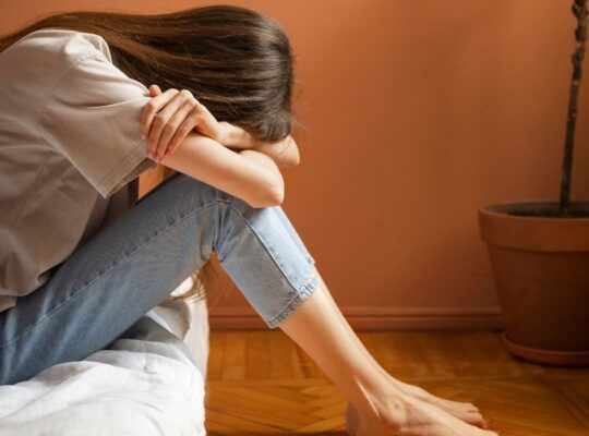 Woman sat on a bed, upset after experiencing betrayal and nervous system disruption